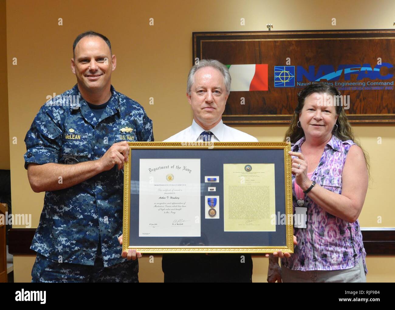 Naval Facilities Engineering Command (NAVFAC) Europe Africa Southwest Asia (EURAFSWA) Commanding Officer Capt. Bob McLean (left) and Laura Haverlock (right), Acquisitions business line coordinator, present Arthur T. Homburg, NAVFAC EURAFSWA senior contracting officer and supervisory contracting specialist, with the Navy Meritorious Civilian Service Award July 1, 2014. During Homburg's six years with NAVFAC EURAFSWA, he was directly responsible for timely acquisition planning and awarding of more than 267 contract actions worth more than $522 million, to include assisting Public Works Departmen Stock Photo