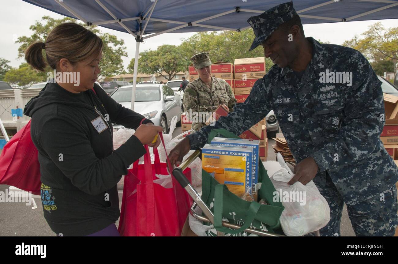 Logistics Specialist 1st Class Jonas Estime helps a shopper with groceries during the Neighborhood Exchange Food Bank Distribution event at the Murphy Canyon Armed Services YMCA (ASYMCA) Headquarters in San Diego. Sailors volunteered with the ASYMCA, who partnered with the San Diego Food Bank, to provide qualifying families with fresh produce and non-perishable items such as bottled juices, cereal and canned stews. Stock Photo