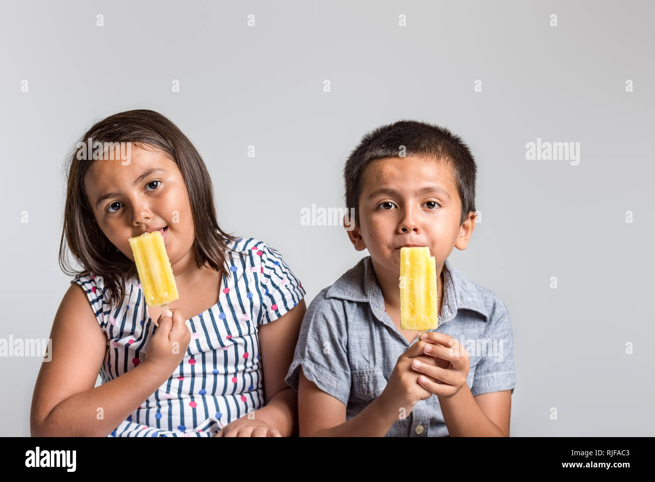 Young boy and girl with natural expression enjoying ice cream, studio image with copy space for text. Stock Photo