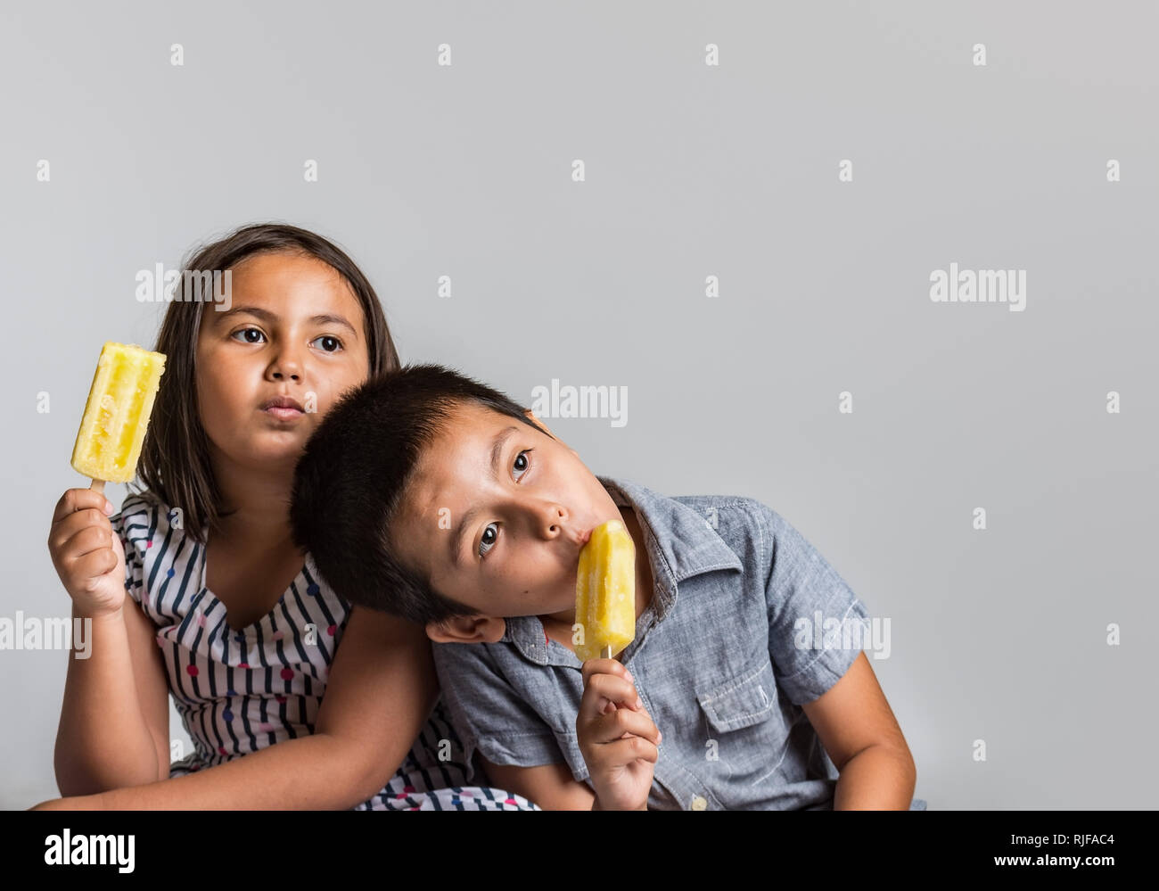 Young boy and girl with natural expression enjoying ice cream, studio image with copy space for text. Stock Photo