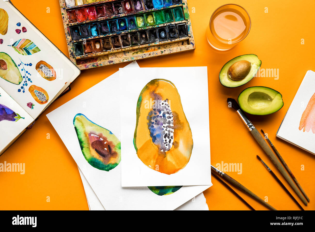 top view of avocado and papaya drawings next to colored paints, paintbrushes on yellow background Stock Photo