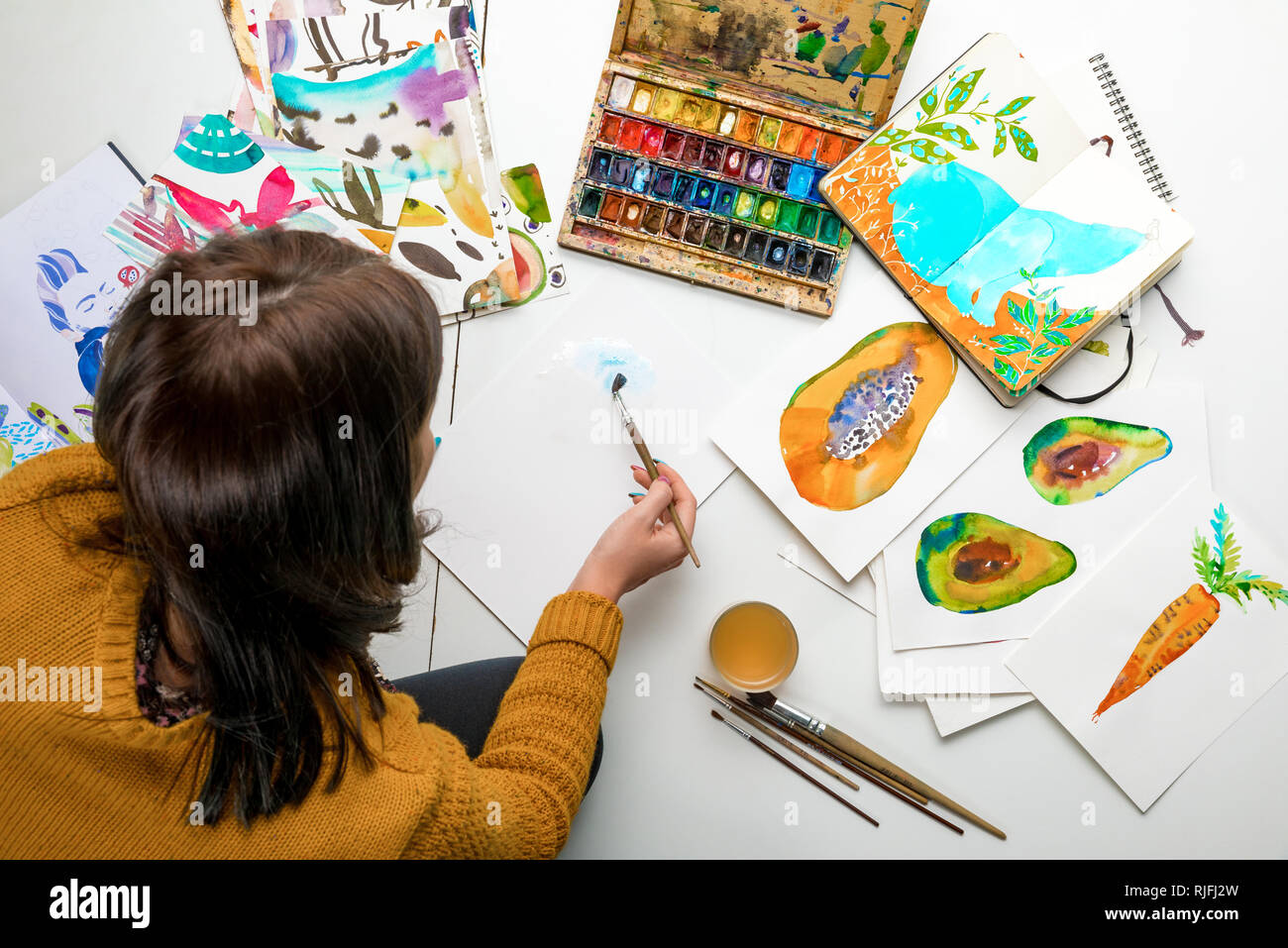 https://c8.alamy.com/comp/RJFJ2W/top-view-of-woman-painting-with-watercolors-paints-while-surrounded-by-color-drawings-and-drawing-utensils-RJFJ2W.jpg