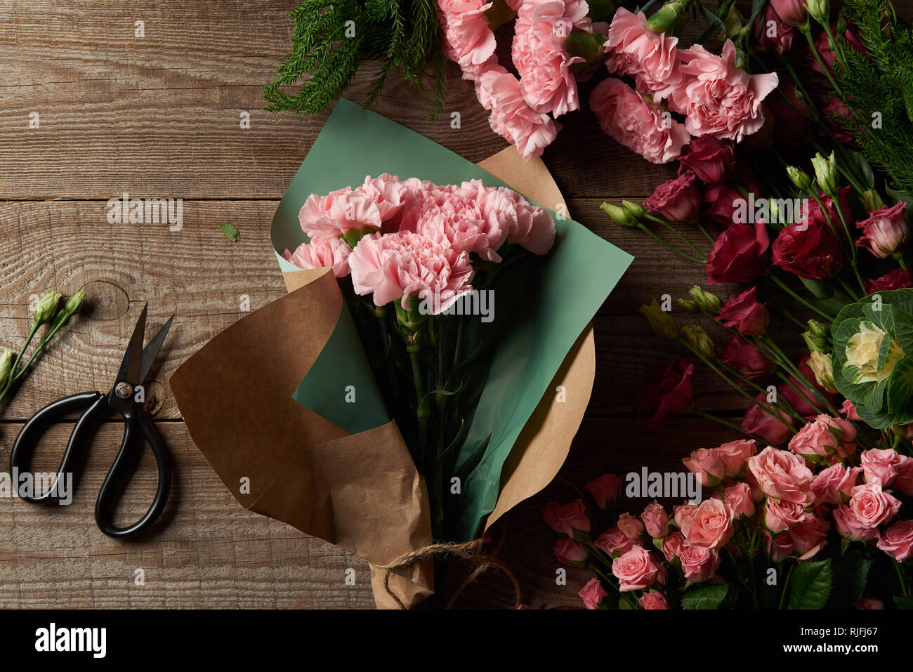 top view of beautiful tender flowers with craft paper and scissors on wooden surface Stock Photo