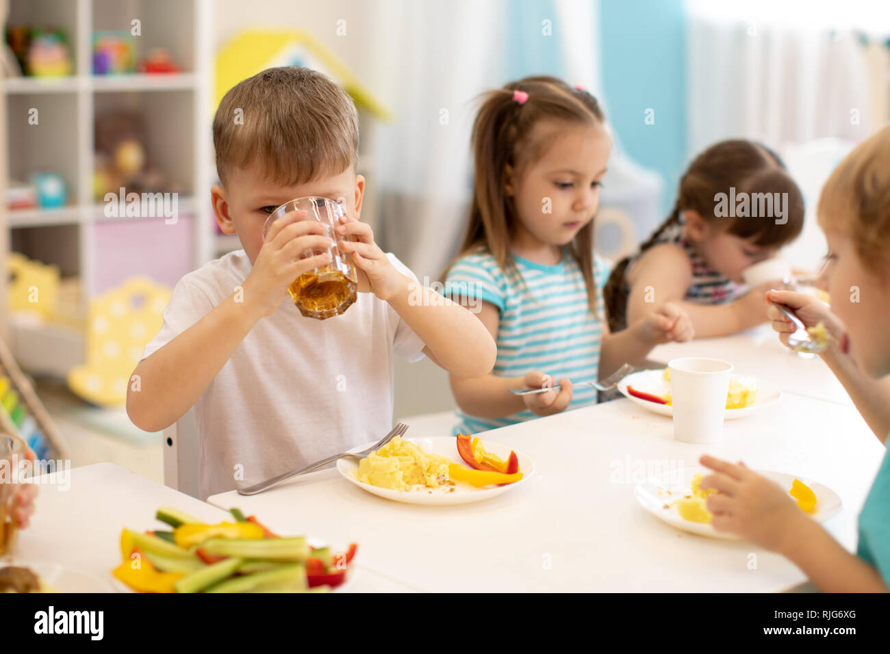 Lunch in daycare. Group of children eat healthy food. Kid boy drinking
