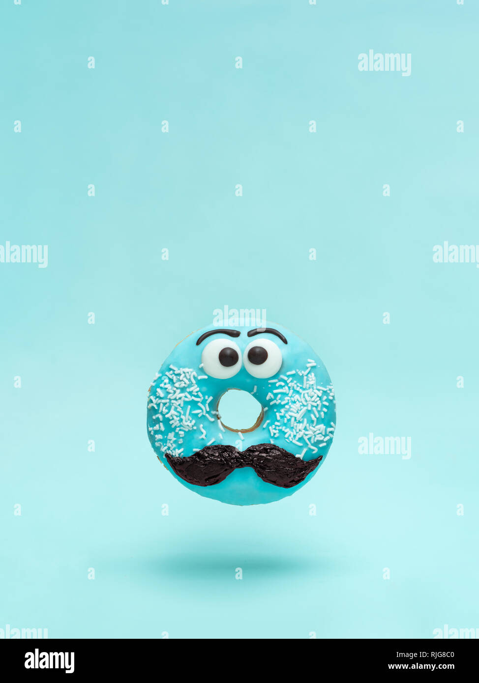 Blue glazed donut with mustache. Flying blue doughnut with funny face with mustache over blue background. Copy space for text. Masculinity or father Stock Photo