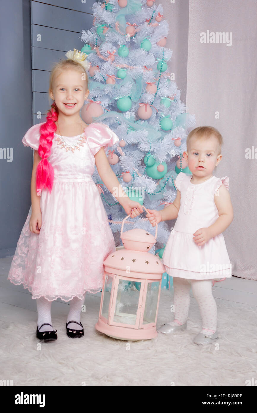 Portrait of a two cute little european blond princess girls with a crown  in a beautiful dress in a studio decorated in the Christmas theme with toys, Stock Photo