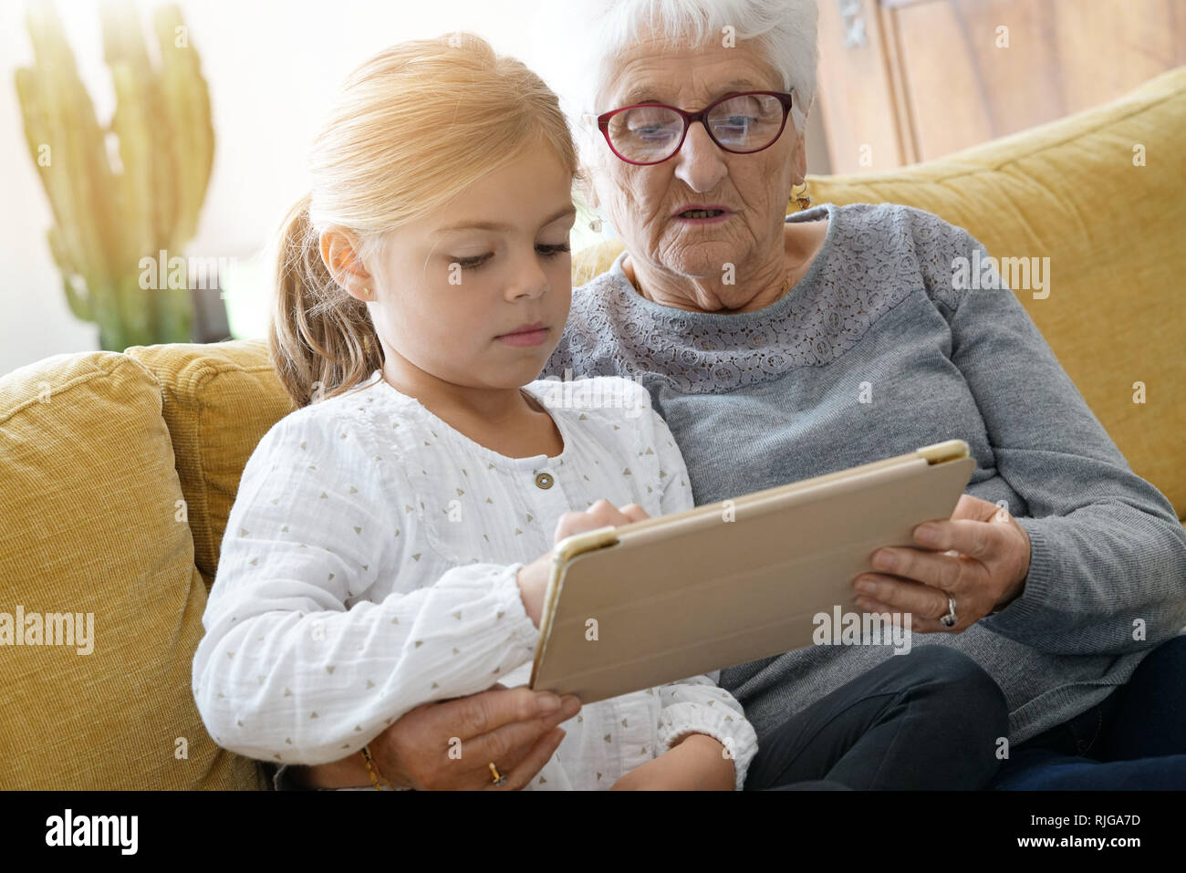 Little girl with grandmother using tablet at home Stock Photo - Alamy