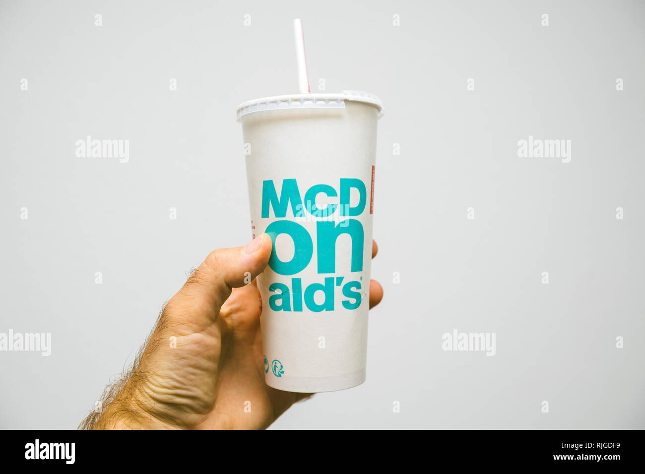 PARIS, FRANCE - JUL 27, 2018: Man holding inside restaurant against white background a cup of McDonald's Cola with plastic straw with blue text Stock Photo