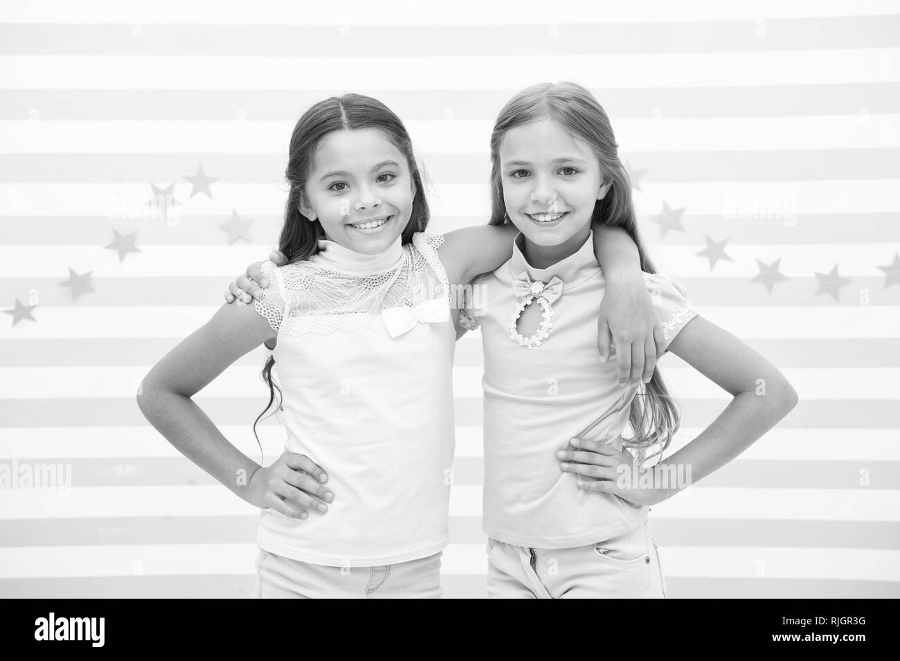 Happy childhood concept. Kids schoolgirls preteens happy together. Friendship from childhood. Girls smiling happy faces hug each other while stand striped background. Girls children best friends hugs. Stock Photo
