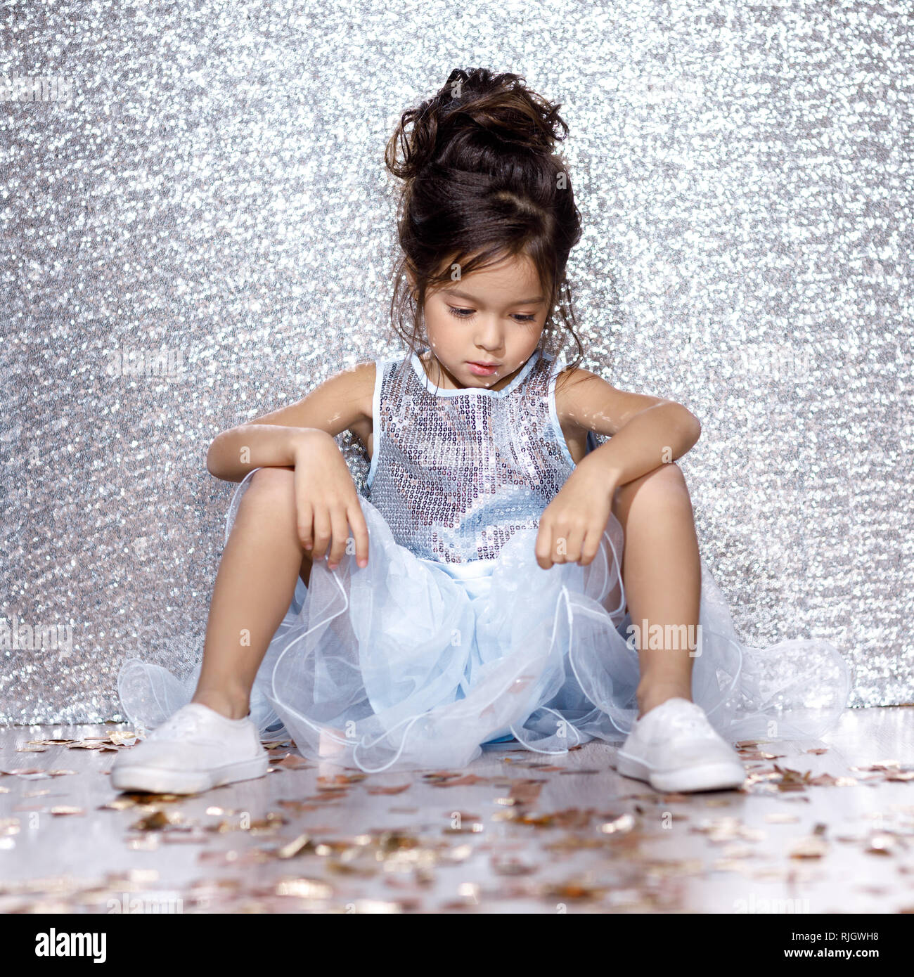 sad little child girl in blue dress sitting on the floor with confetti on  background with silver bokeh. after birtday party Stock Photo - Alamy