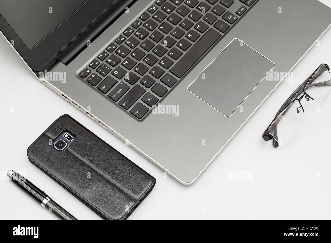 Workspace composition of laptop computer, smartphone pen, and folded glasses on office desk table background.  Stacked focus image. Stock Photo