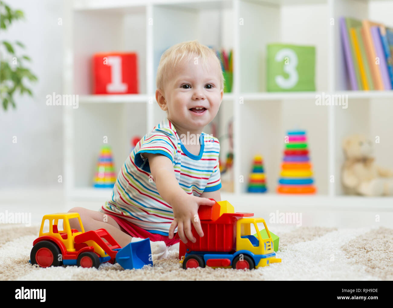 Little child plays with toy cars. Kid boy sitting on the floor at home ...