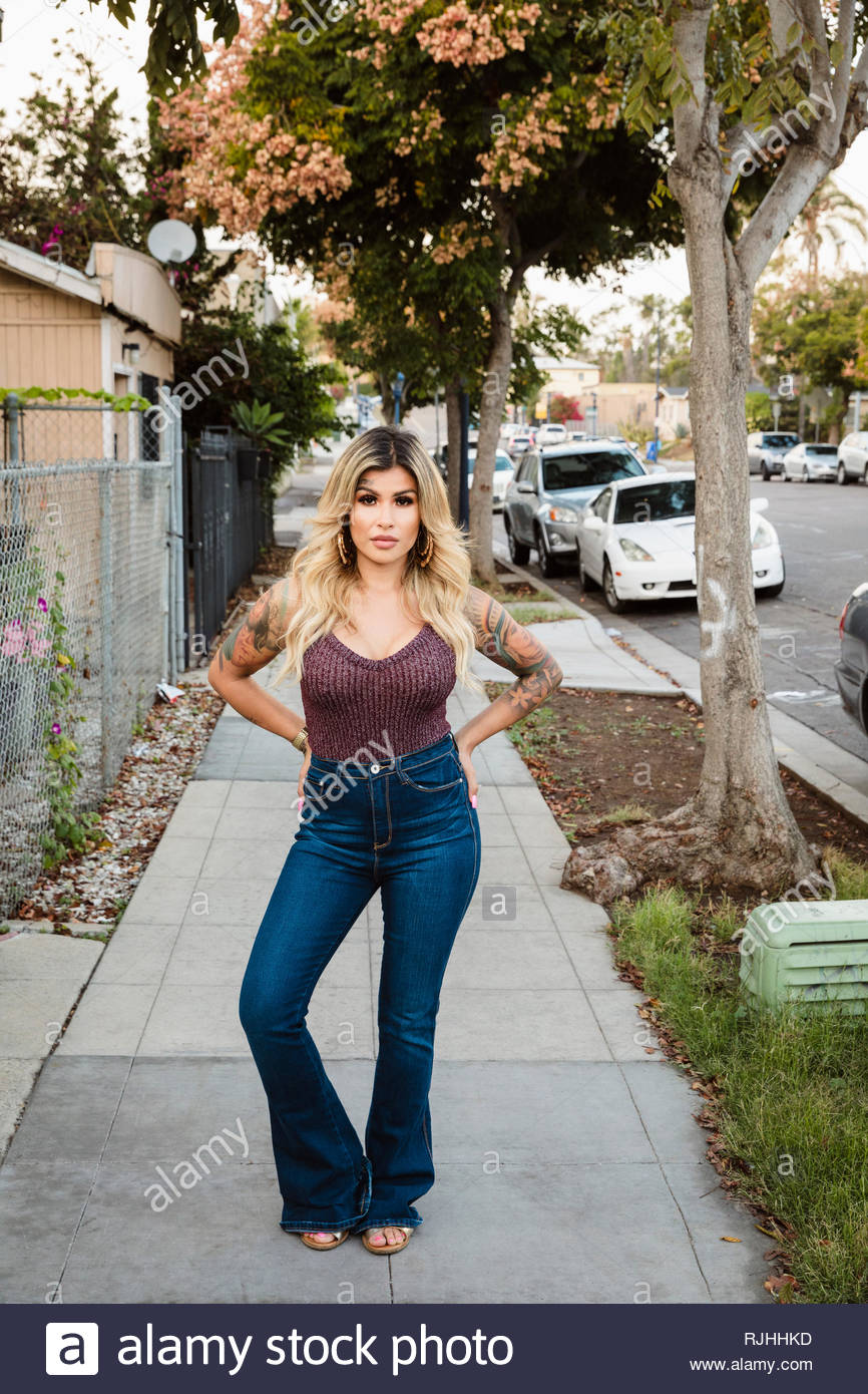 Portrait confident, tough Latinx young woman with tattoos on neighborhood sidewalk Stock Photo