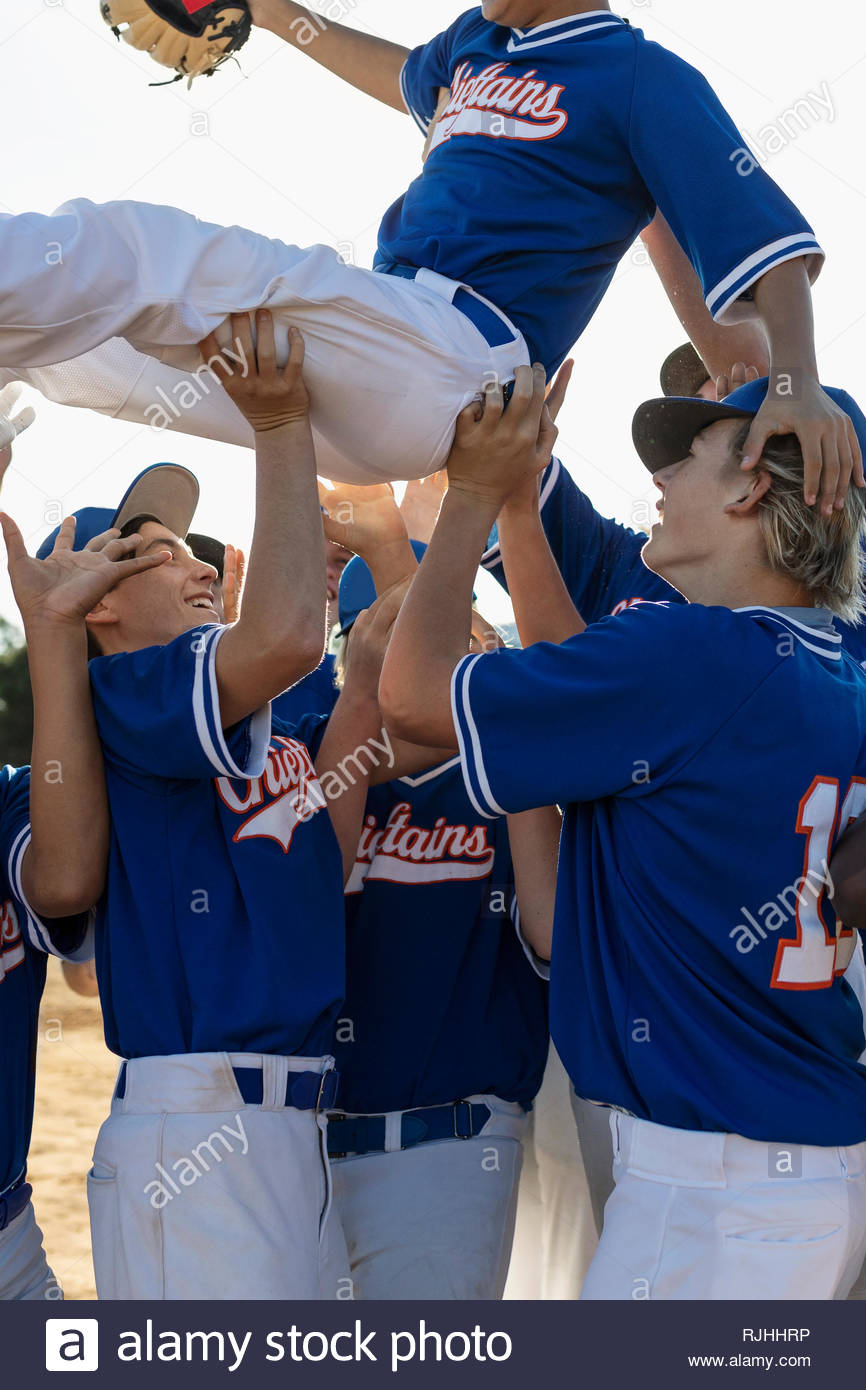 Excited baseball players celebrating, carrying teammate overhead Stock Photo