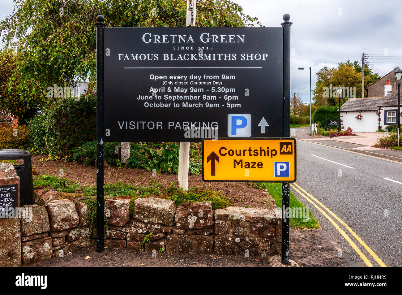 A large black notice board at the entrance to Gretna Green famous blacksmiths shop, with white lettering advertising and giving times of  opening Stock Photo