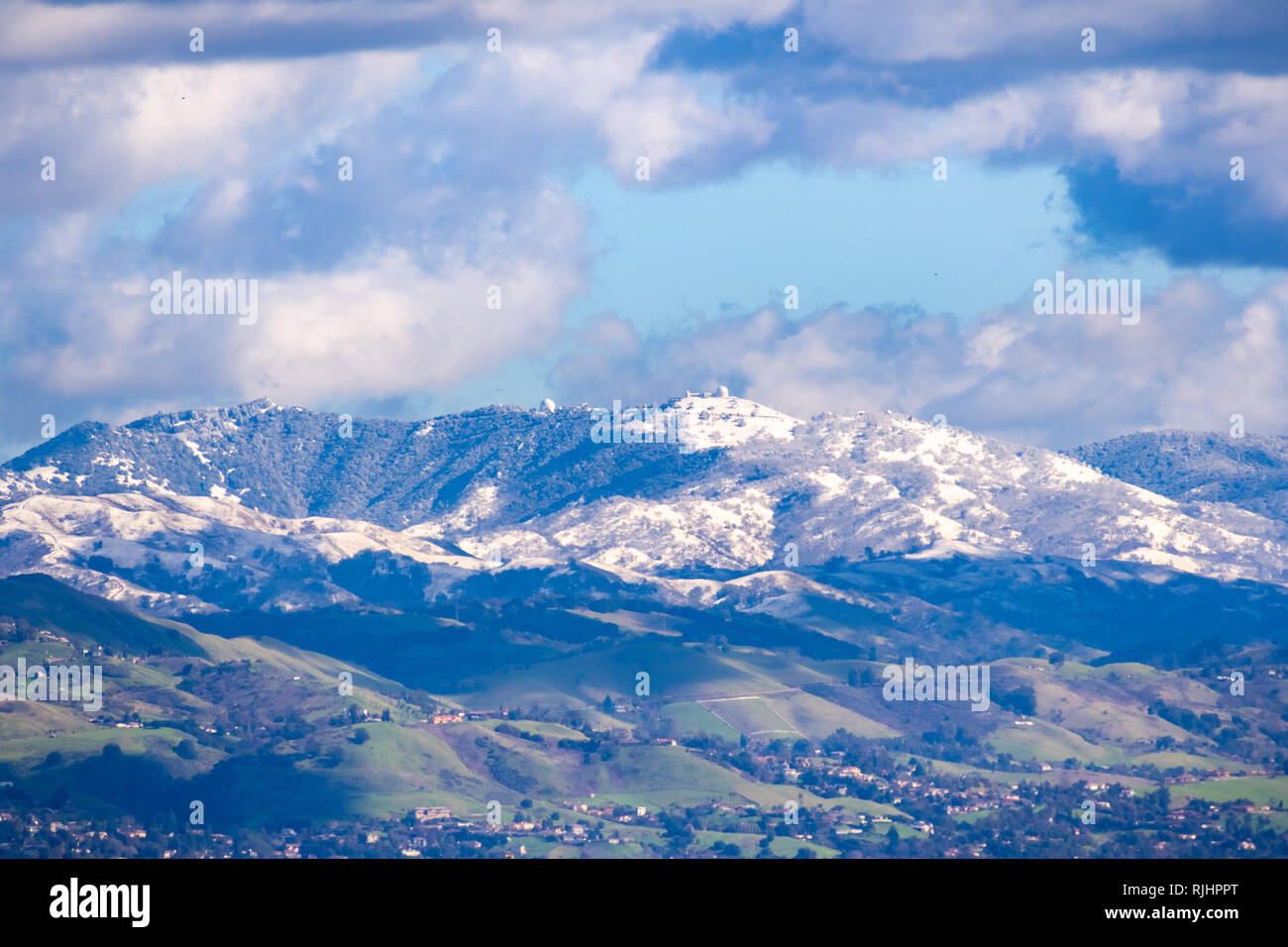 View towards Mt Hamilton and the Lick Observatory building on a sunny winter day; green hills in the foreground and snow covered peaks in the backgrou Stock Photo