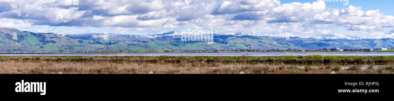 Panoramic view towards green hills and snowy mountains on a cold winter day taken from the shores of a marsh in south San Francisco bay area; San Jose Stock Photo