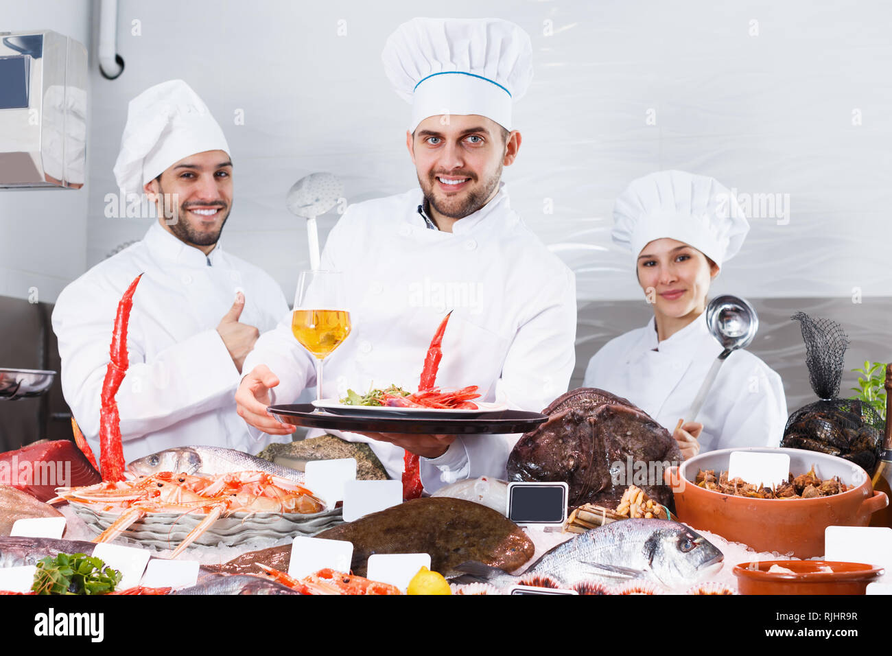 Smiling group of professional cooks of fish restaurant inviting to