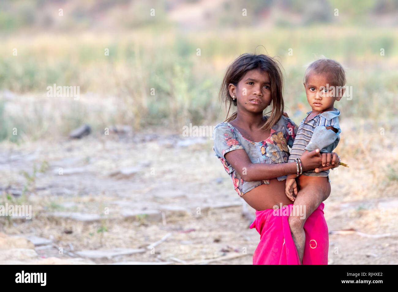 A young girl from the Bhil tribe holds a younger male in rural Rajasthan near Bhainsrorgargh, India. Stock Photo