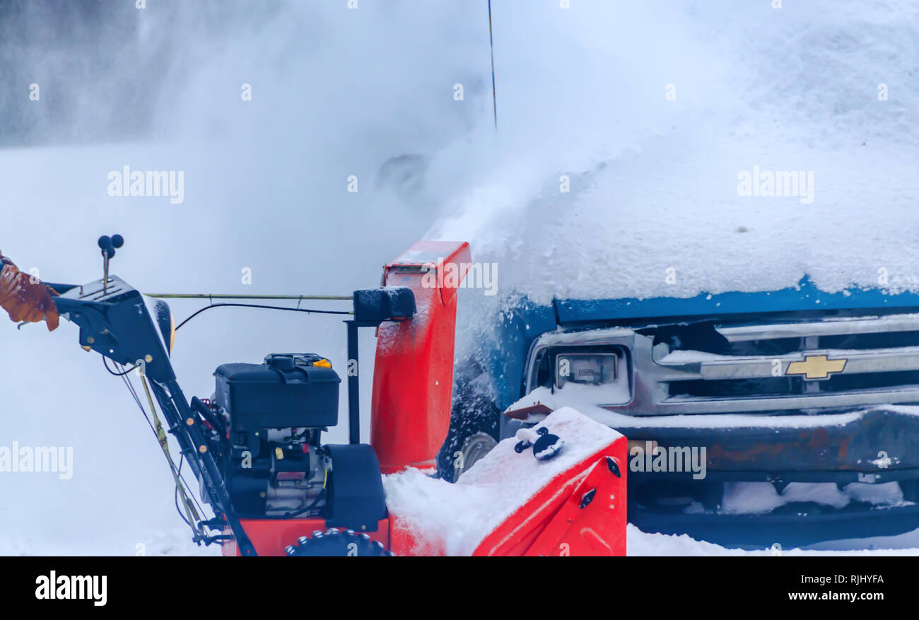 Winter weather. Snow gushing out of a snow blower and burying a Chevy truck parked in a parking lot of an apartment complex in Michigan, USA. Stock Photo