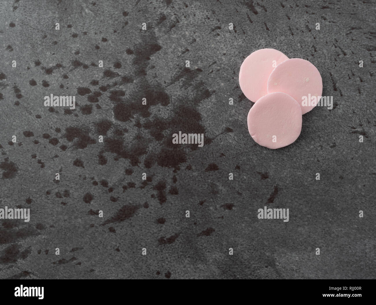 Top view of three pink flavor round candy wafers on a gray background