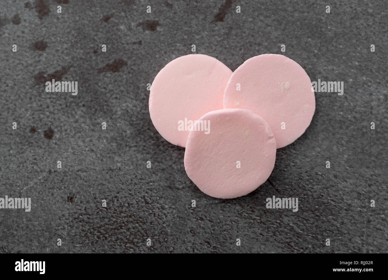 Top view of three pink flavor round candy wafers on a gray background