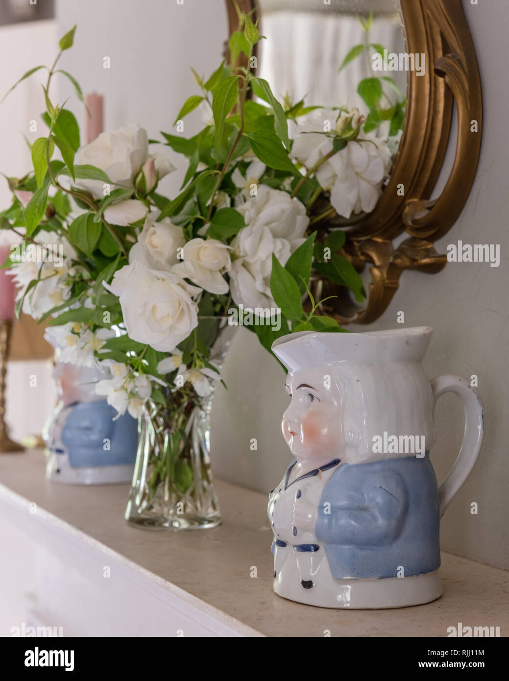 Toby jugs and cut white roses on mantlepiece Stock Photo