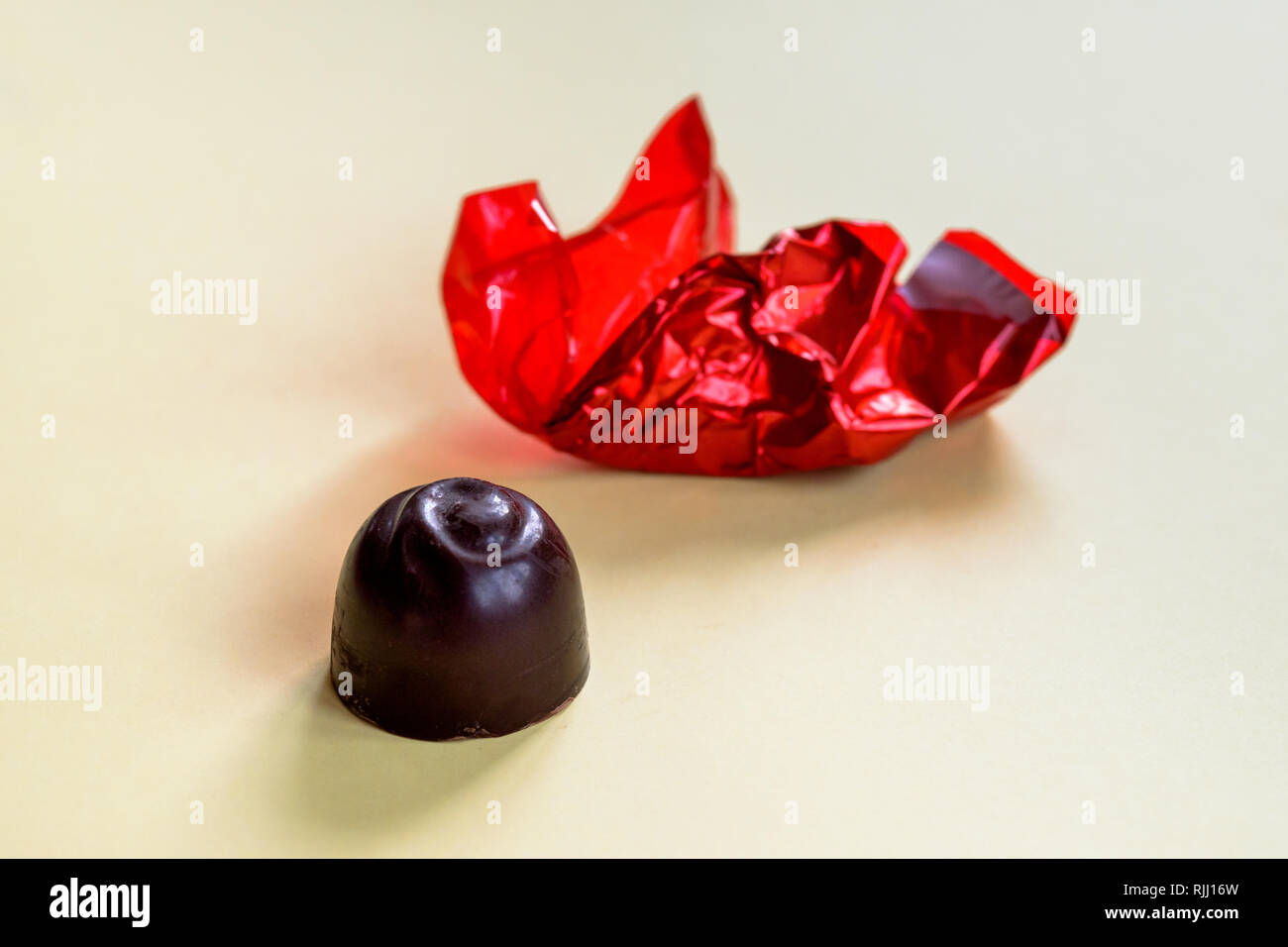 An unwrapped chocolate cherry bonbon with the wrinkled red wrapping paper and isolated on a yellow background. Stock Photo