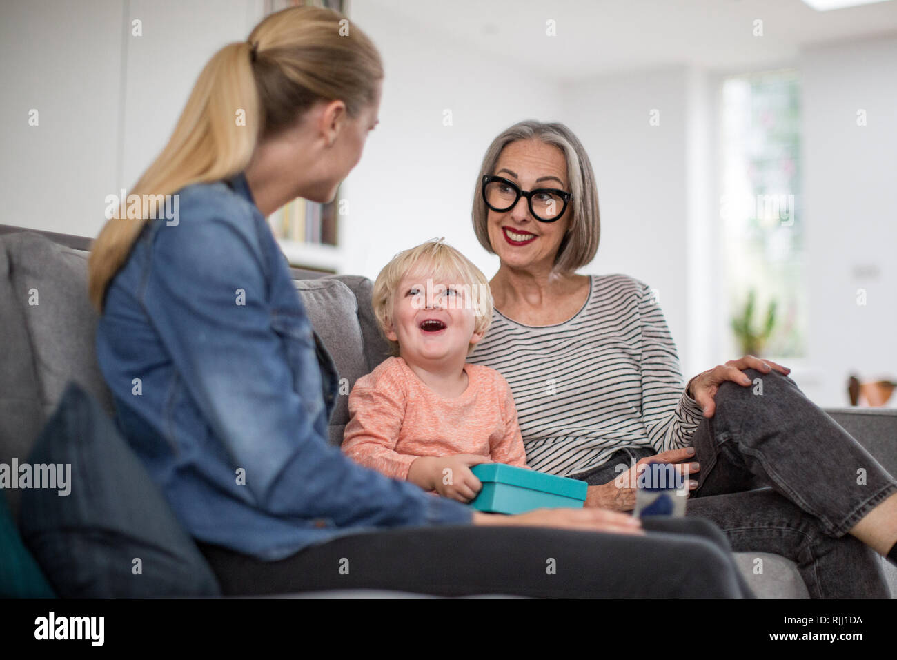 Boy opening a birthday present with grandmother and mother Stock Photo