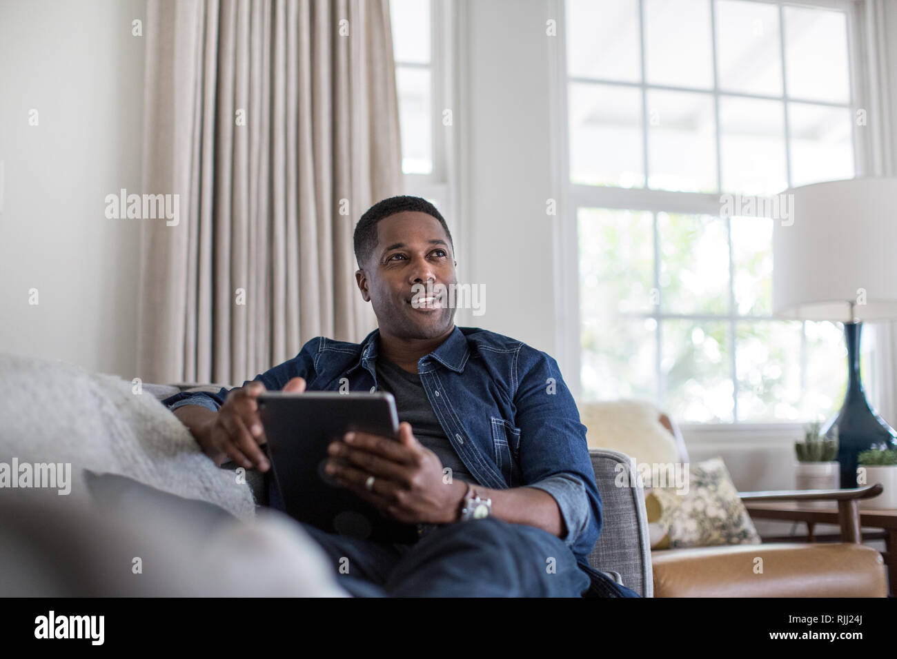 African American adult male using digital tablet at home on sofa Stock Photo