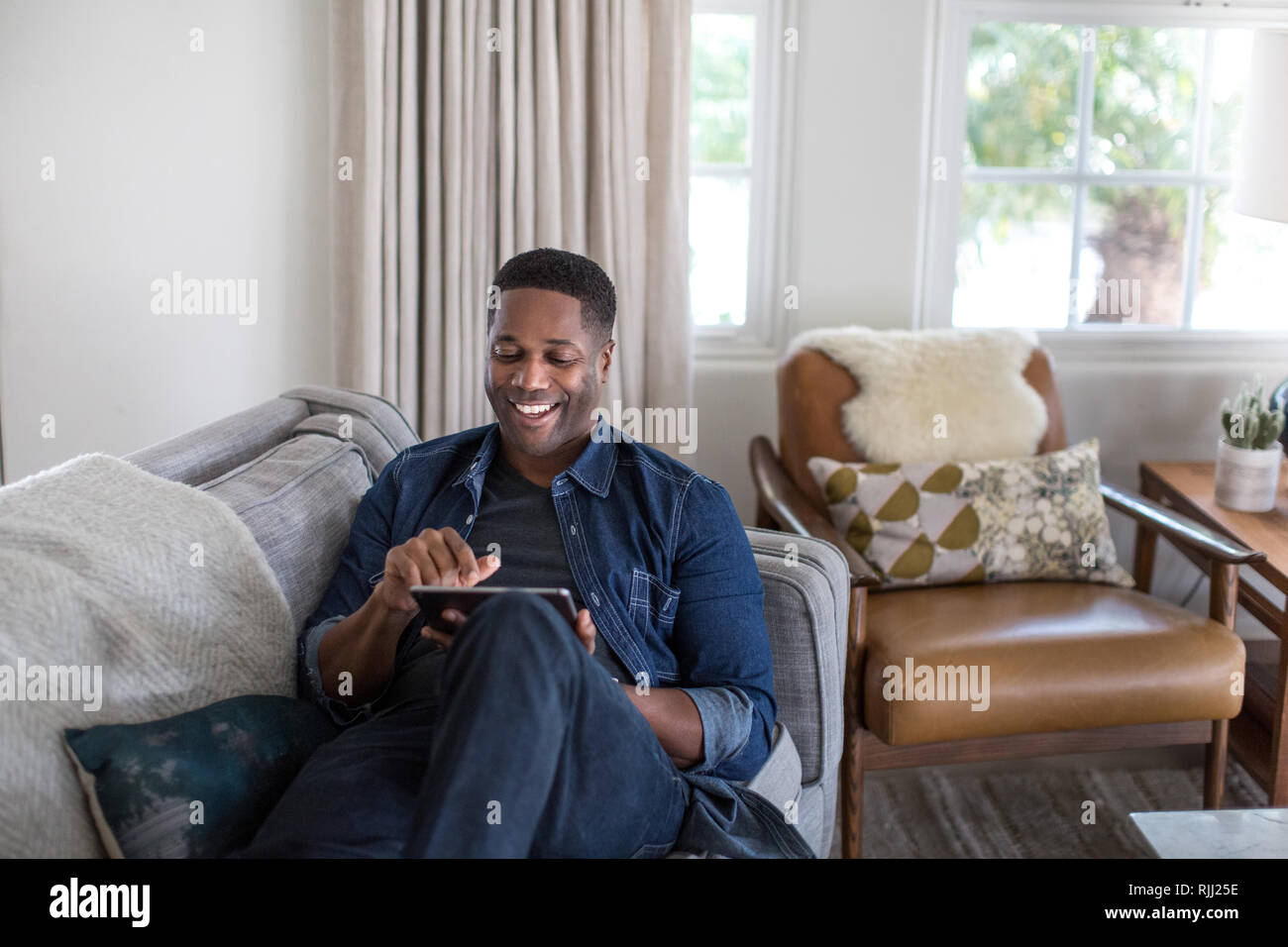 African American adult male using digital tablet at home on sofa Stock Photo