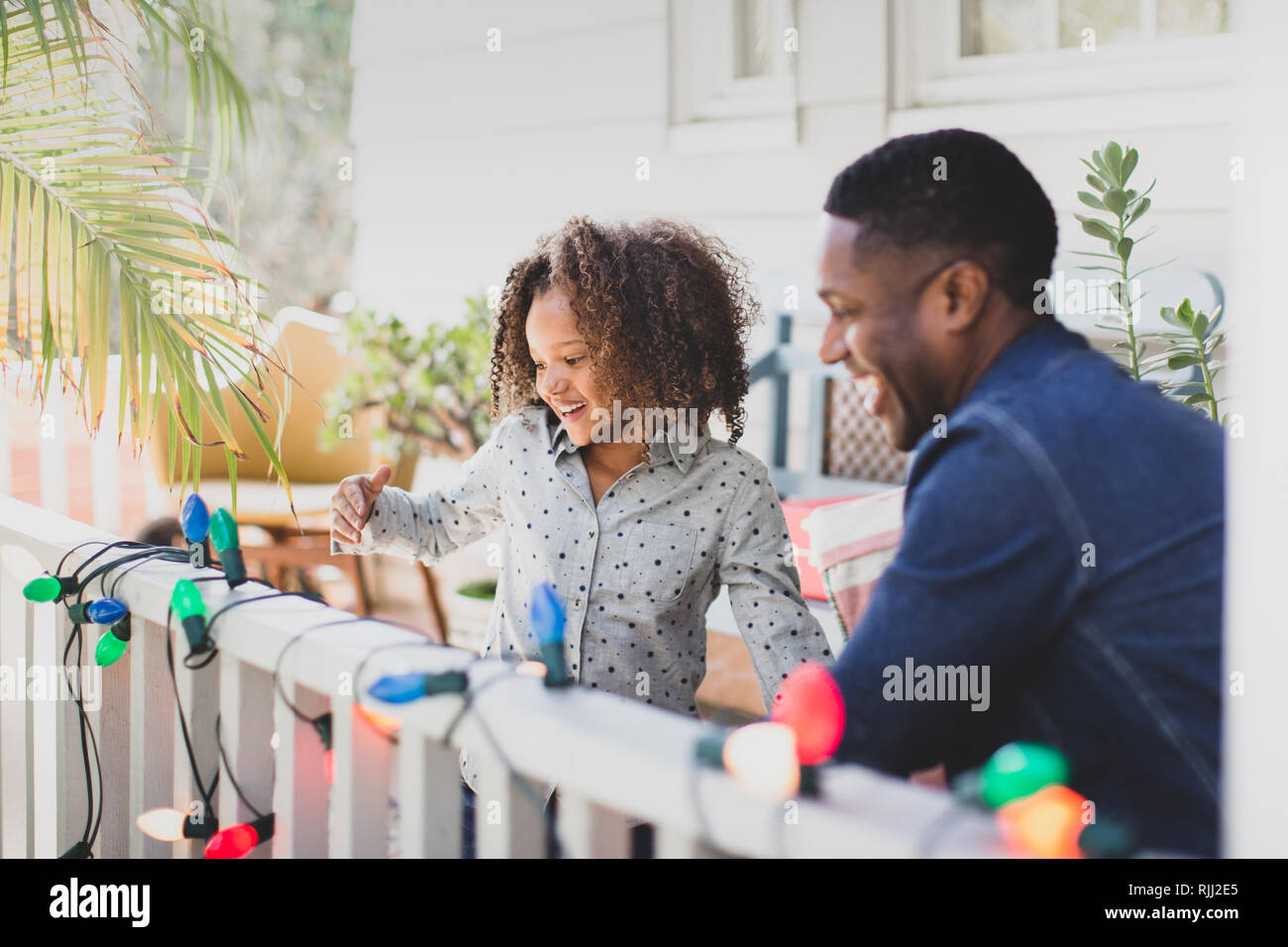 African American father and daughter hanging christmas lights outdoors Stock Photo