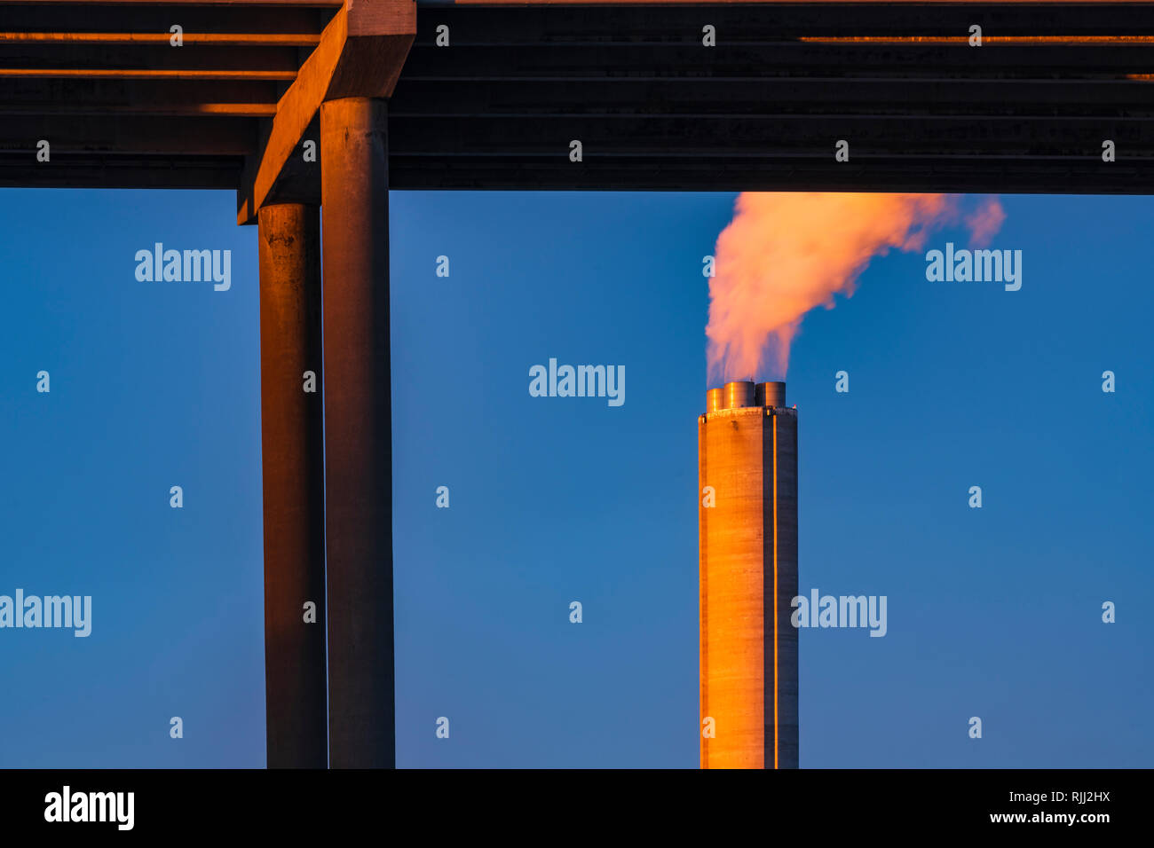 Industrial chimney by bridge billowing smoke into blue sky, low angle view, horizontal image, Gothenburg, Sweden, Europe Stock Photo