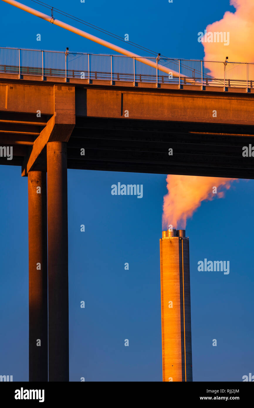 Industrial chimney by bridge billowing smoke into blue sky, low angle view, vertical image, Gothenburg, Sweden, Europe Stock Photo