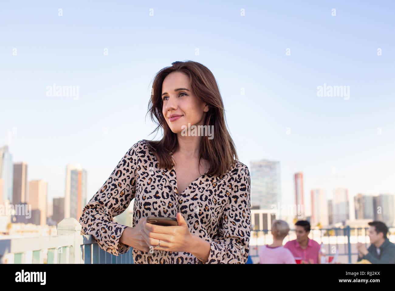 Young adult female looking out across city at a rooftop party Stock Photo