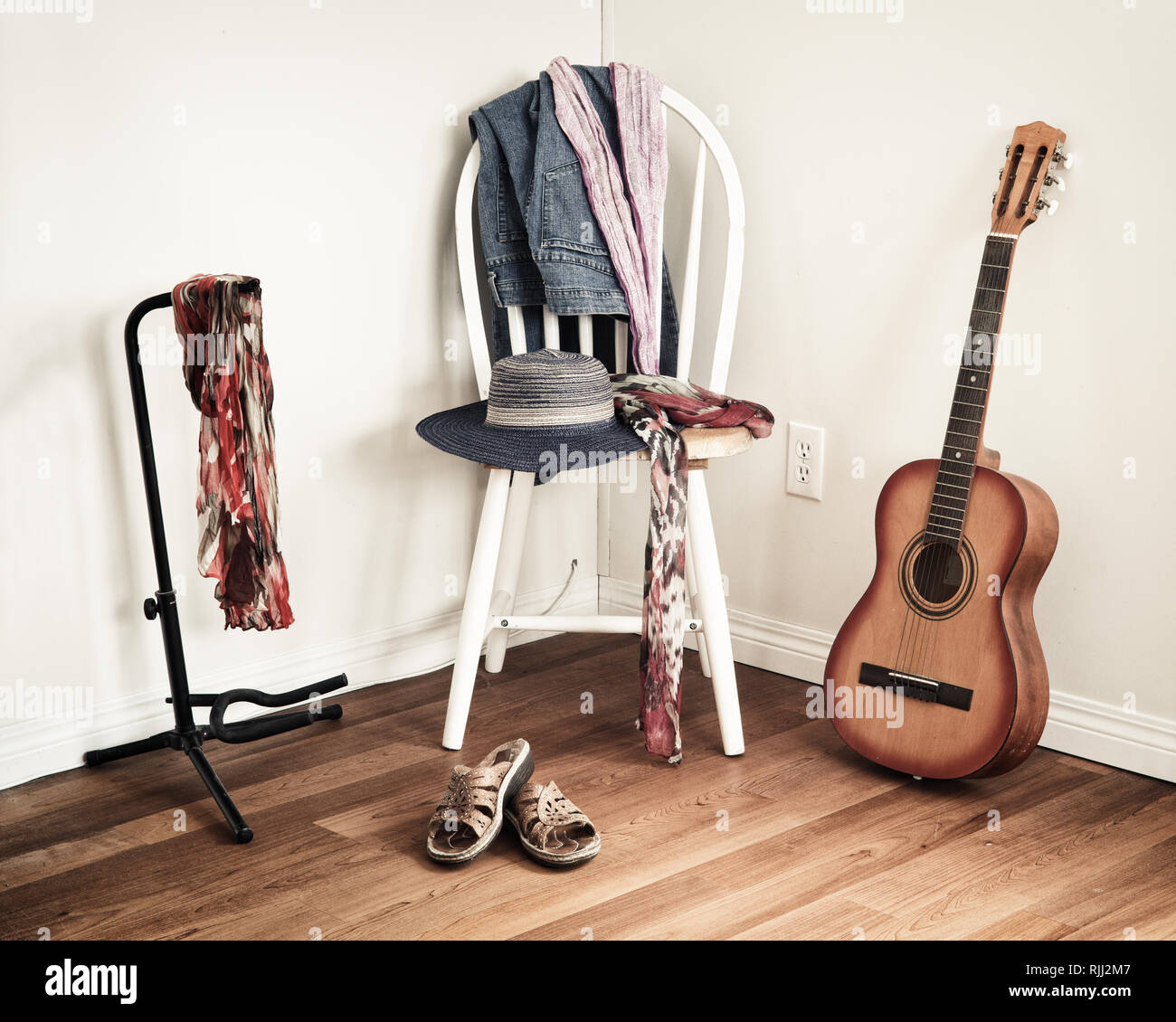 Women's casual clothing on chair in domestic setting with acoustic guitar leaning against wall. Stock Photo