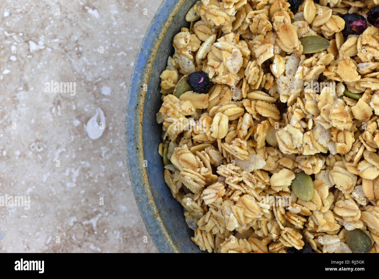Top close view of a bowl of dry organic breakfast cereal with dried blueberries and pumpkin seeds on a marble table. Stock Photo