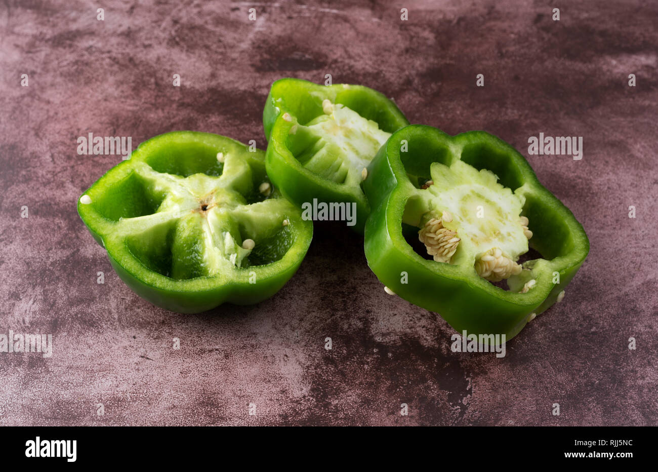 Side view of three slices of green bell pepper on a maroon counter top. Stock Photo