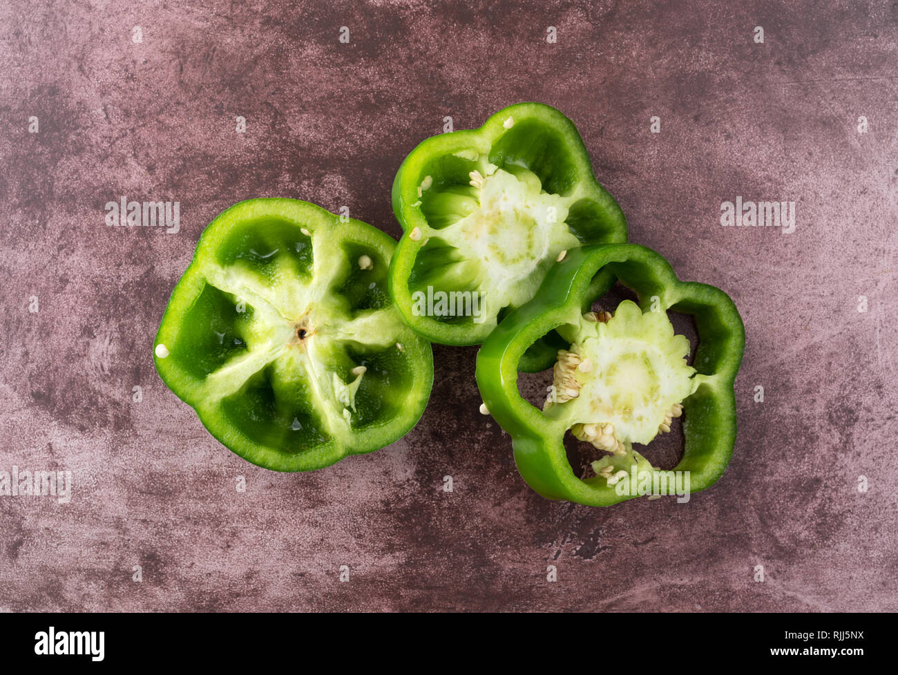 Top view of three slices of green bell pepper on a maroon counter top. Stock Photo