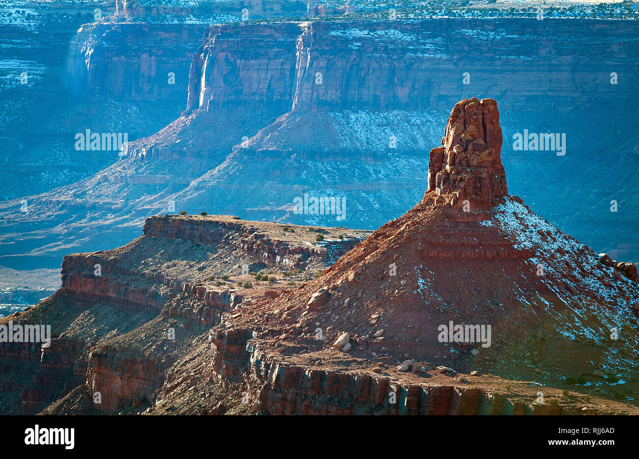 January 2019: A towering spire above the snow covered red sandstone walls and White Rim Trail, Canyonlands National Park, Moab, Utah. Stock Photo