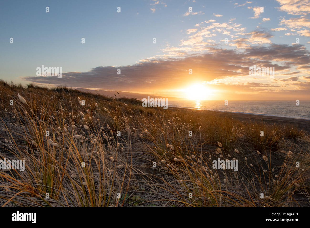 The sun rises over the ocean and Kaitorete Spit warming up the landscape in Canterbury, New Zealand Stock Photo