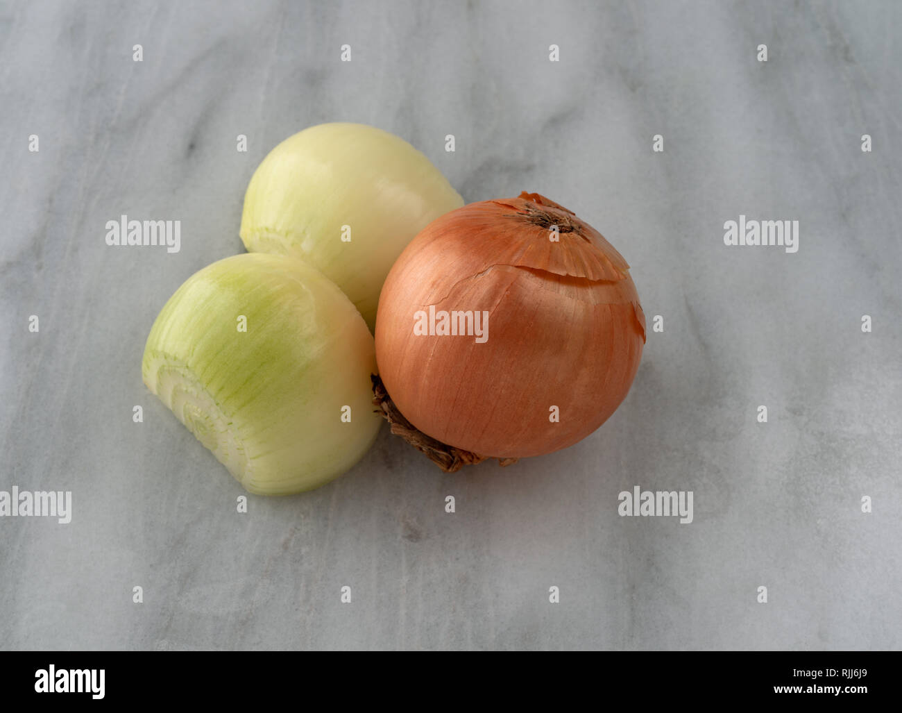 Side view of a whole yellow onion and one cut in half on a gray marble