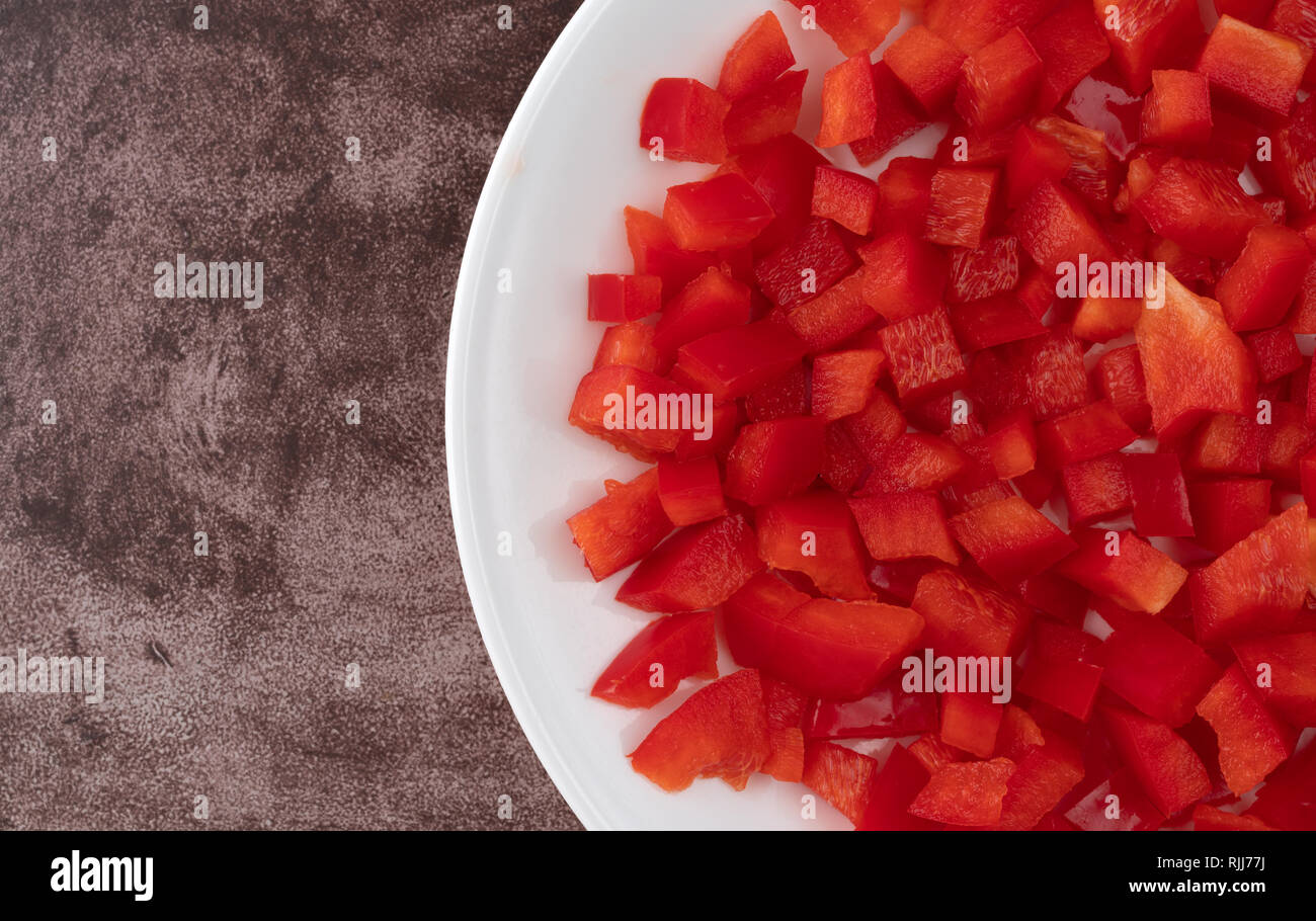 Top view of chopped red bell peppers on a white plate atop a maroon counter top. Stock Photo
