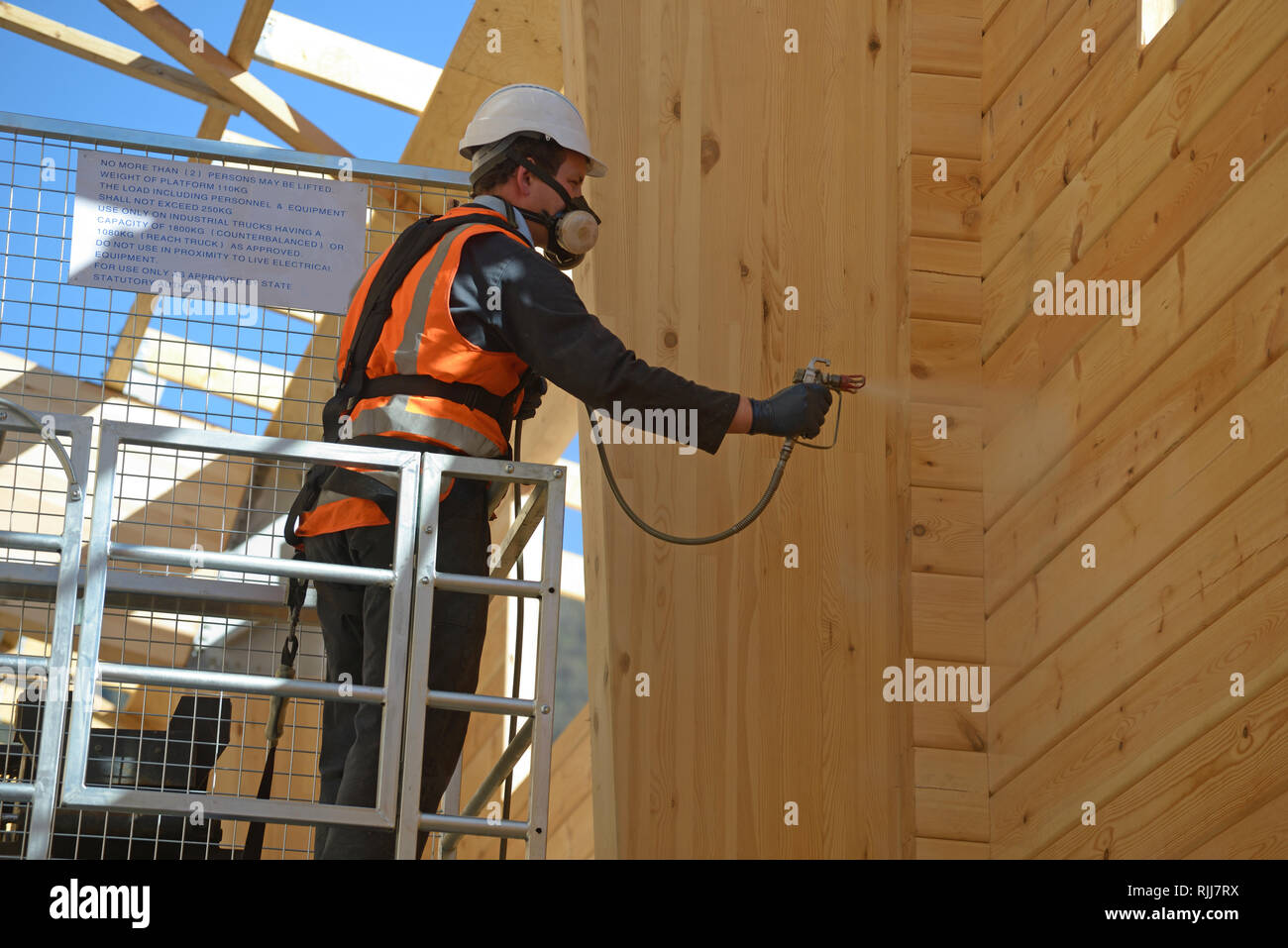Tradesman spray painting the wall of a wooden industrial building with timber preservative Stock