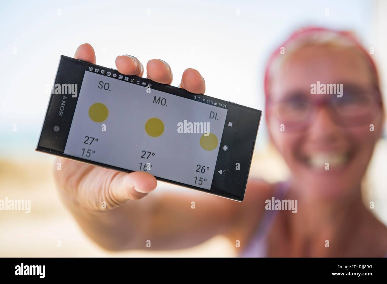 Laughing woman on the beach happy about sunny weather in the weather forecast on her smartphone, Normandie, France Stock Photo