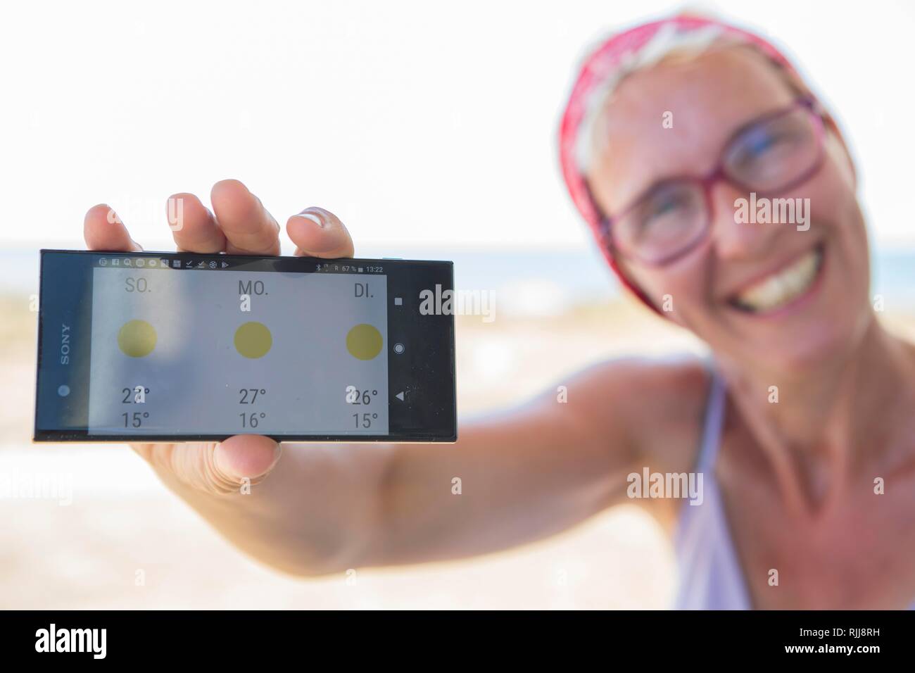 Laughing woman on the beach happy about sunny weather in the weather forecast on her smartphone, Normandie, France Stock Photo