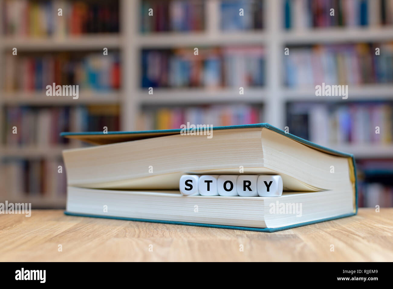 Dice in a book form the word 'story'. Book is lying on a wooden desk in a library. Stock Photo