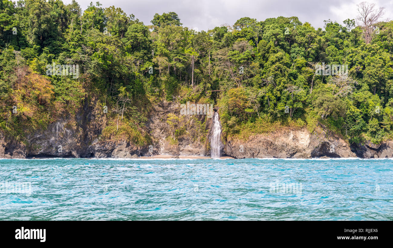 A landscape photo of a lovely waterfall flowing over a cliff at the beautiful tropical coast of Corcovado National Park, Costa Rica. Stock Photo