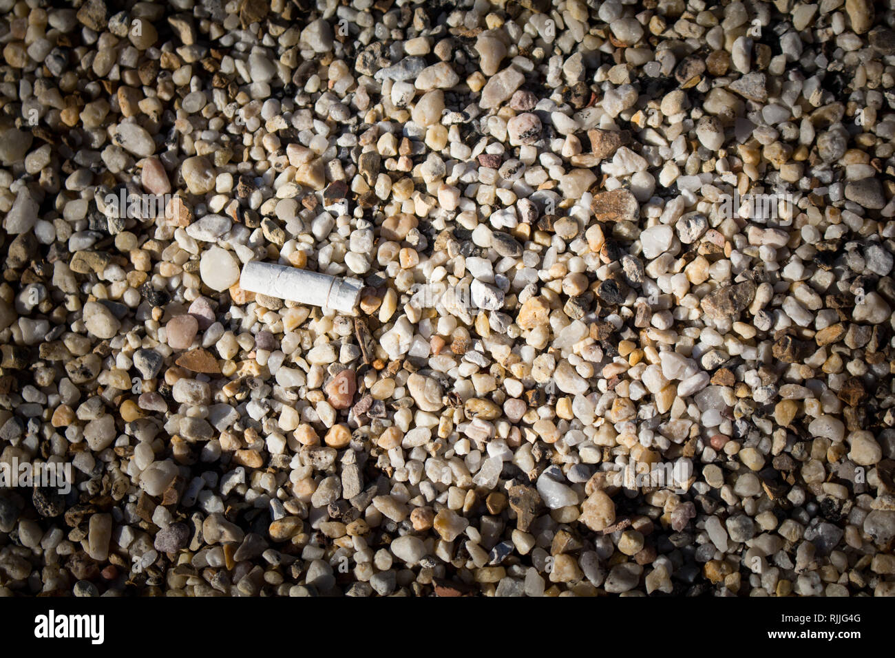 A cigarette discarded on a pebbled ground. Stock Photo