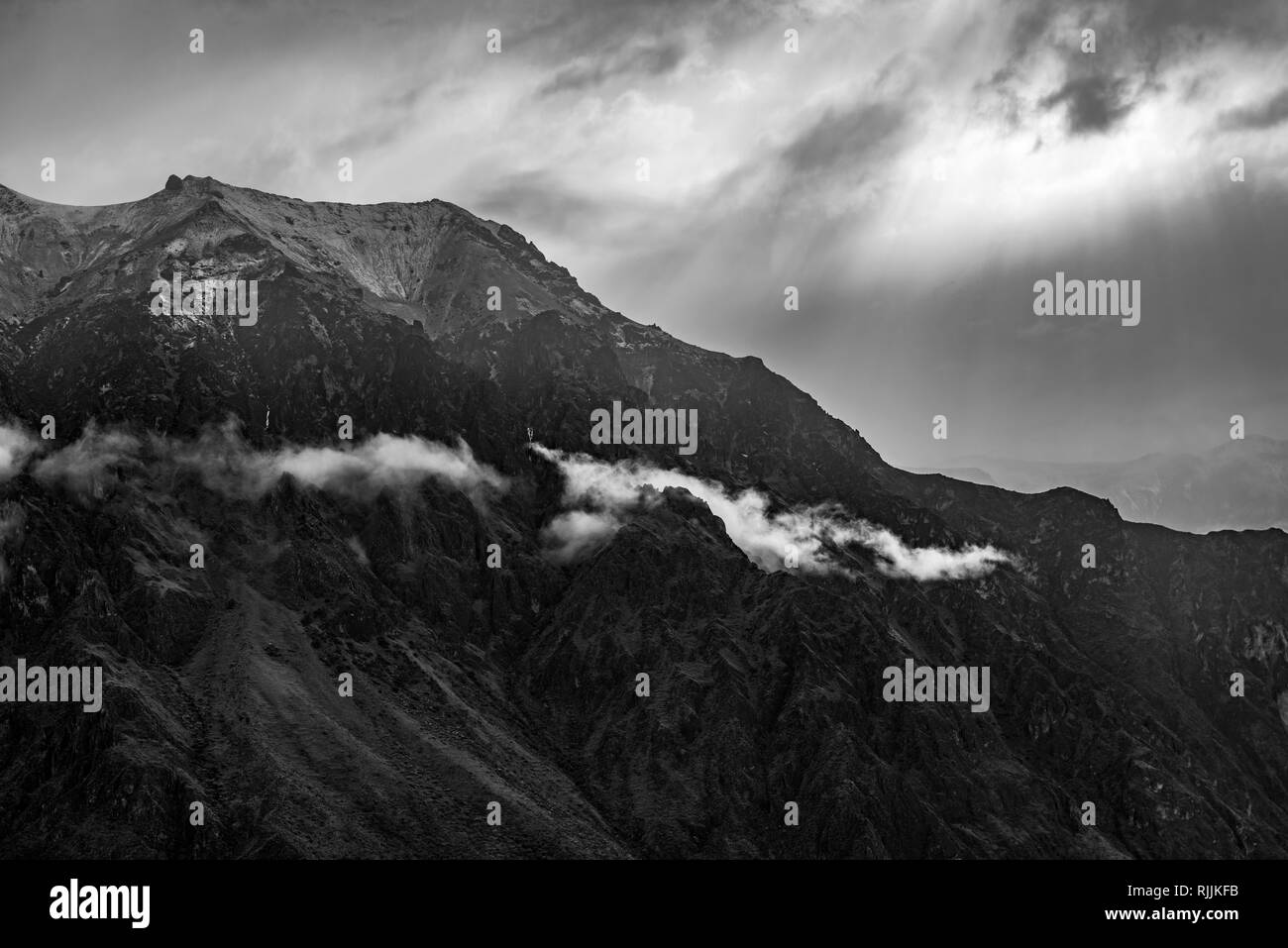 The Andes mountain range in black and white as sunlight illuminates the peaks and clouds near the Colca Canyon, Arequipa, Peru. Stock Photo